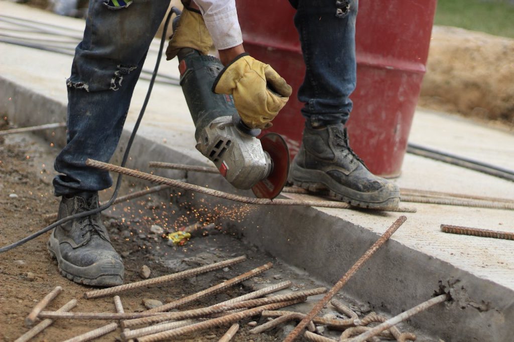 Close-up of a worker using an angle grinder to cut steel bars on a construction site.
